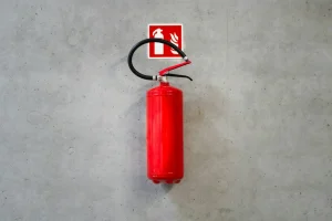 Extintor de incendios rojo colgado en una pared de concreto con señalética. Fotografía de Jakub Zerdzicki.